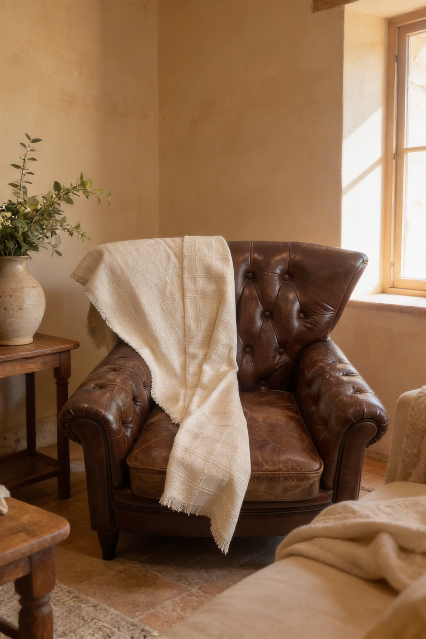 Manta tejida beige decorando un sillón de cuero en un ambiente cálido y acogedor.