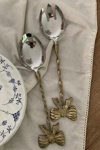 Set de dos servidoras de metal con detalle de lazo dorado y mangos texturizados para servir ensaladas y acompañamientos.
