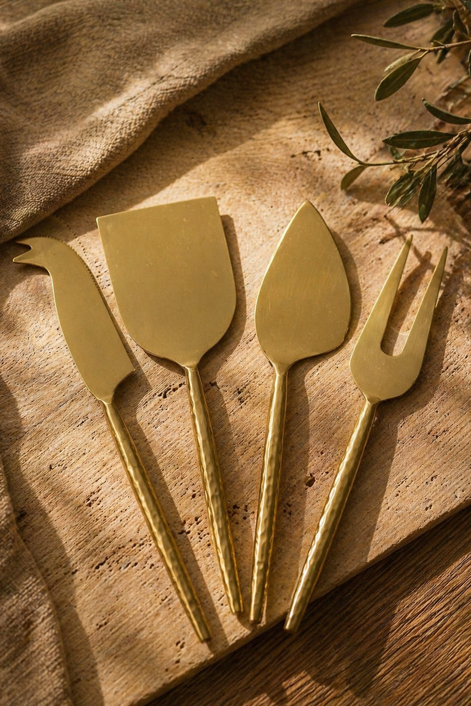 Set de cuatro utensilios dorados para cortar y servir queso sobre una tabla de madera.